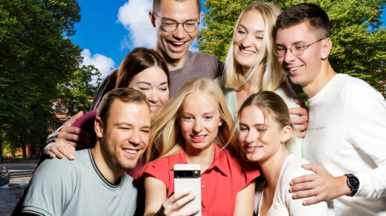 Sieben junge Menschen machen ein Gruppenselfie auf dem Rostocker Universitätsplatz.
